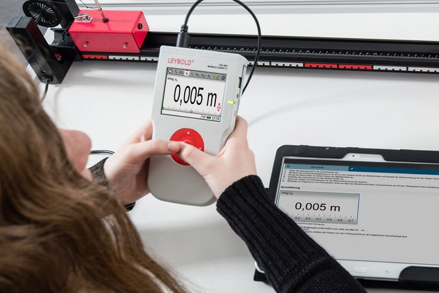 Eine Schülerin im Physikunterricht führt die Messung im Experiment mit dem Schülermessgerät Mobile-CASSY 2 WLAN durch. Die digitale Versuchsanleitung Lab Docs zeigt den gleichen Messwert im Lab Docs wie das Schülermessgerät an. 