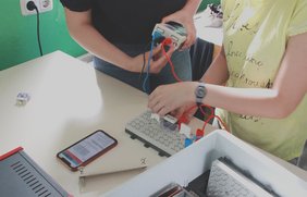 Die Schülerinnen und Schüler des Markgraf-Albrecht-Gymnasiums in Osterburg bauen einen Science Lab Schülerversuch einfach und schnell mit der digitalen Versuchsanleitung Lab Docs, die auf dem Handy gezeigt wird, auf. Sie schließen gerade das Mobile-CASSY-2 WLAN an. 