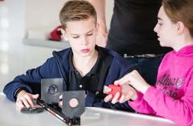 Die Lehrkraft der Gesamtschule Hürth erläutert den Schülerinnen und Schülern im Physikunterricht ein Experiment zum Thema Fernrohrmodell aus dem Schülerversuchesystem Science Lab. 