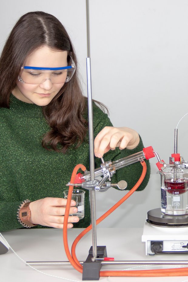 Beim diesem Science Lab Schülerversuch aus der Organischen Chemie führt eine Schülerin eine Destillation von Wein durch, um Ethanol zu erhalten. Sie trägt dafür eine Schutzbrille.