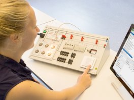 Schülerin arbeitet an einem Schülerarbeitsplatz aus dem Bereich der Gebäudesystemtechnik. Die digitale Versuchsanleitung ist auf eiem Computer sichtbar. 