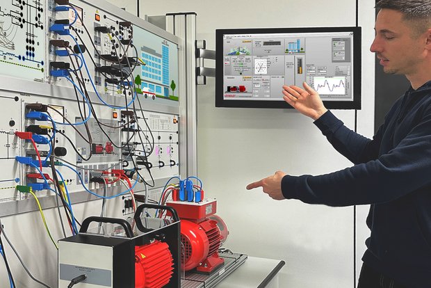 Das Smart Grid Trainingssystem zeigt das Szenario des Stromausfalls in einem Krankenhaus auf einem Monitor. Ein Student zeigt mit einer Hand auf den Generator und mit der anderen Hand auf den Bildschirm.