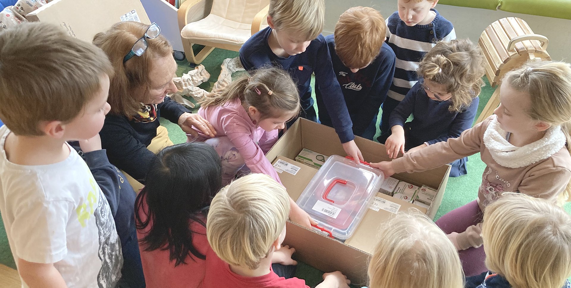 Die Kinder der Kita St. Raphael packen neugierig einen Karton mit verschiedenen Gegenständen aus.