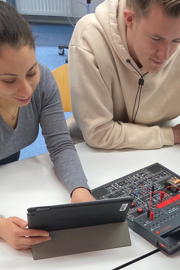 Zwei Schüler*innen arbeiten gemeinsam in Gruppenarbeit am COM4LAB-Arbeitsplatz. Die digitale Versuchsanleitung wird am Tablet bearbeitet.