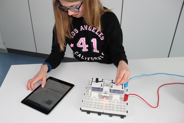 Die Schülerin führt ein Experiment aus der Physik mit dem Science Lab Schülerversuche-System aus. Sie beschäftigt sich mit Wechselschaltungen aus dem Bereich der Elektrischen Grundschaltungen, Stromkreis und Schalter. Es wird ein Beispiel aus dem Alltag verwendet. Die digitale Versuchsanleitung zum Schülerversuch wird auf einem Tablet verwendet.