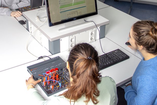 Zwei Schülerinnen experimentieren mit einem COM4LAB-Kurs flexible an einem Computer. Die digitale Versuchsanleitung ist gut sichtbar.